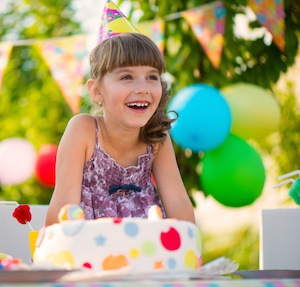 Little girl at a birthday party with a cake and balloons
